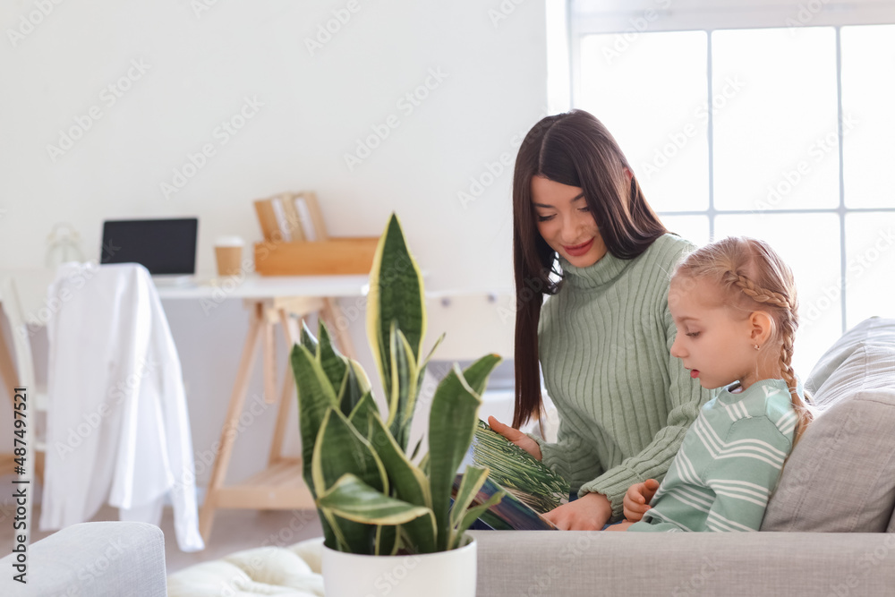 Happy little girl and her mother in warm sweaters reading book at home