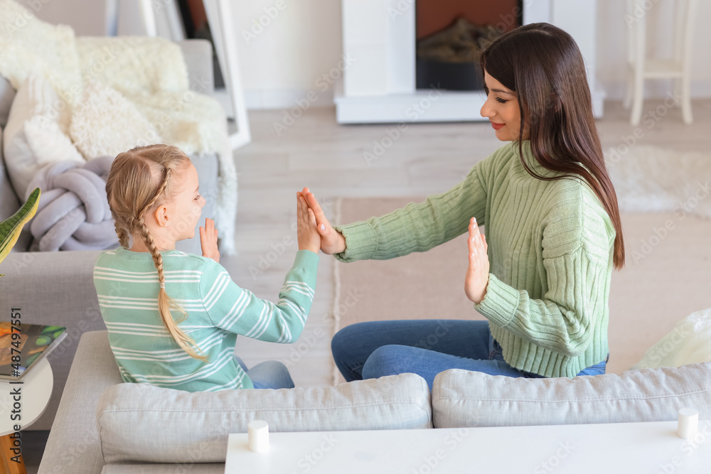 Happy little girl and her mother in warm sweaters playing patty-cake at home