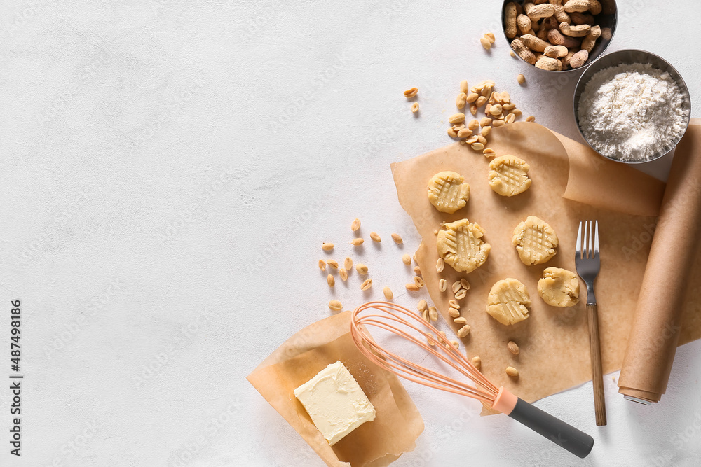 Parchment paper with uncooked peanut cookies and ingredients on white background