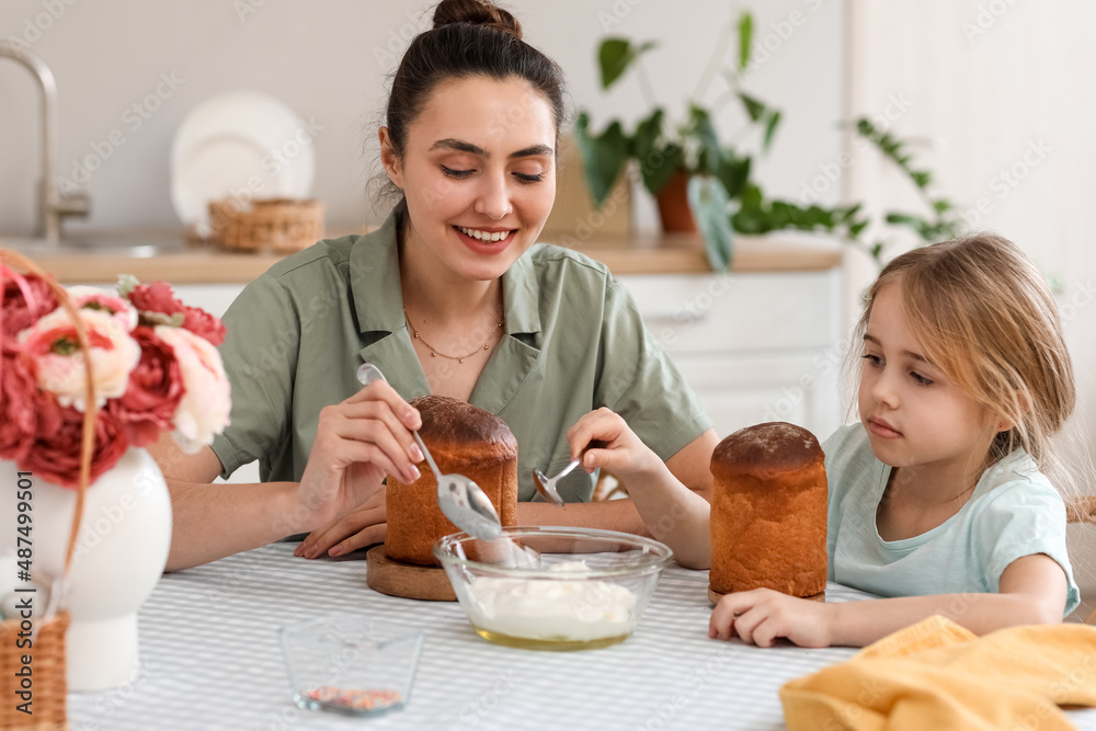 Little girl and her mother glazing Easter cakes in kitchen