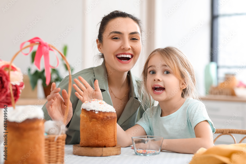 Little girl and her mother with tasty Easter cakes in kitchen