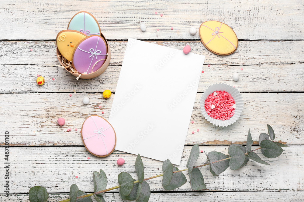 Composition with tasty Easter cookies, eggs, eucalyptus branch and sheet of paper on white wooden ba