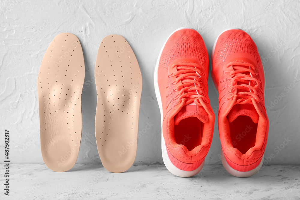 Orthopedic insoles and sneakers on light background