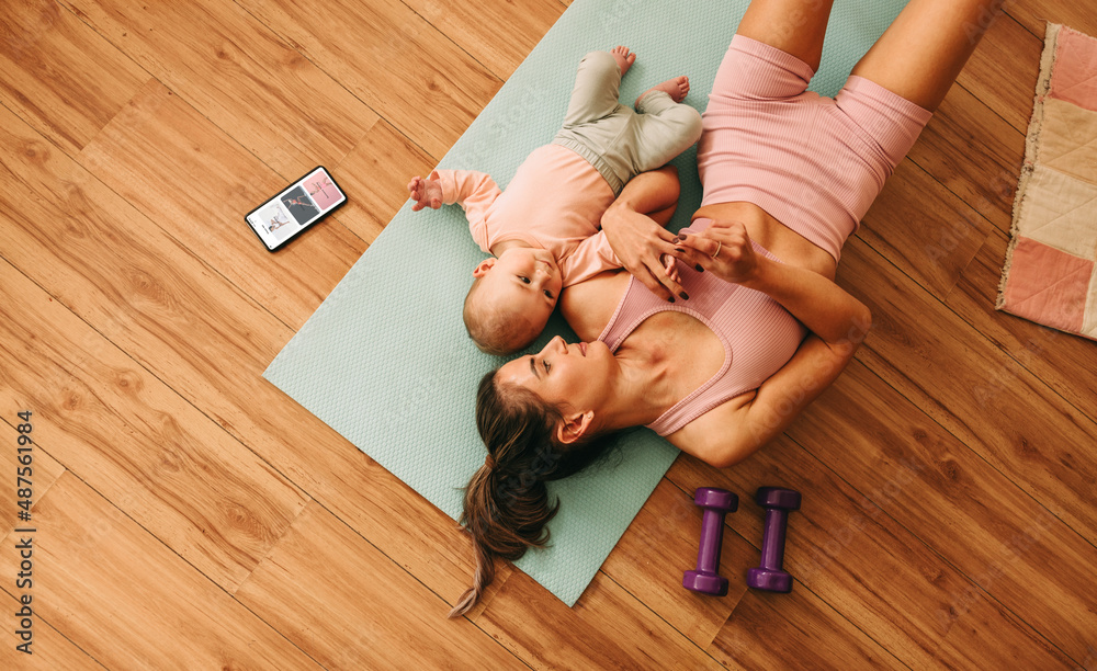 Overhead view of a mom lying on an exercise mat with her baby