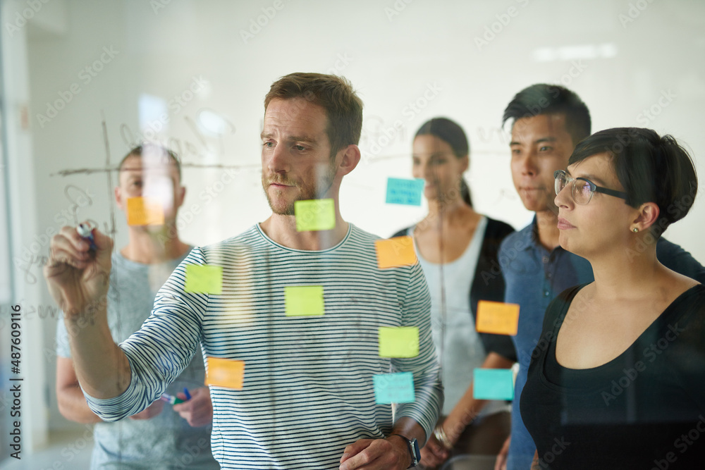 Planning is the first step. Cropped shot of a group of young designers planning on a glass board.