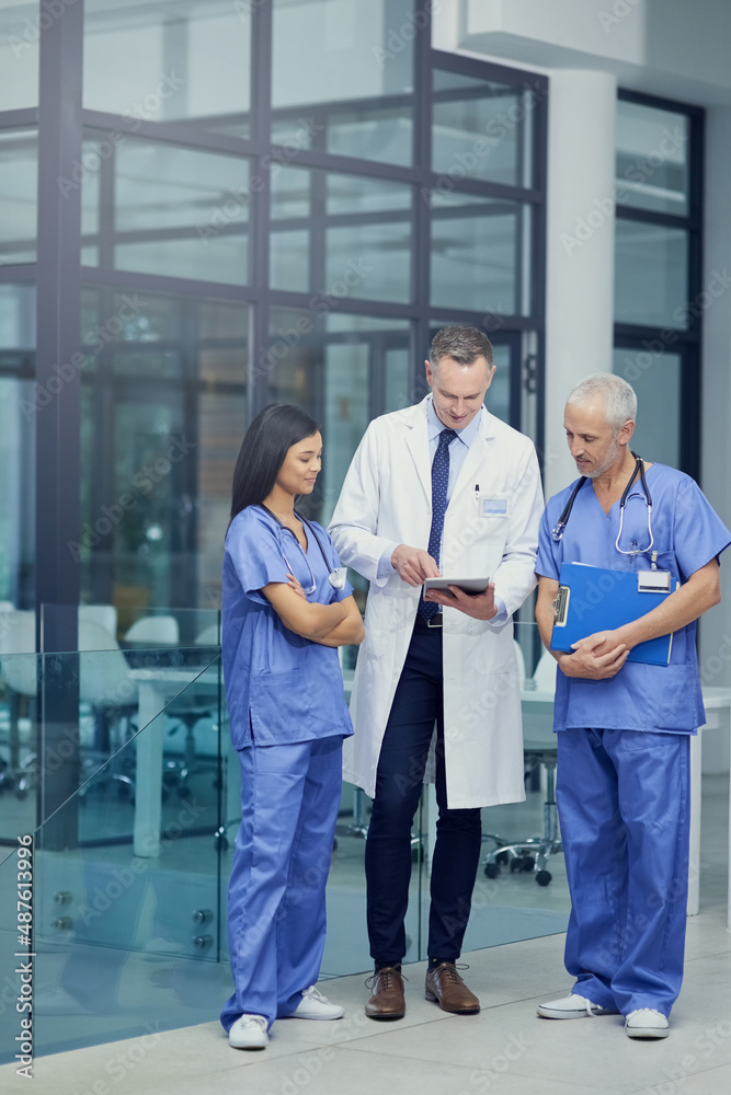 Comparing diagnosis. Shot of a group of doctors talking together over a digital tablet while standin