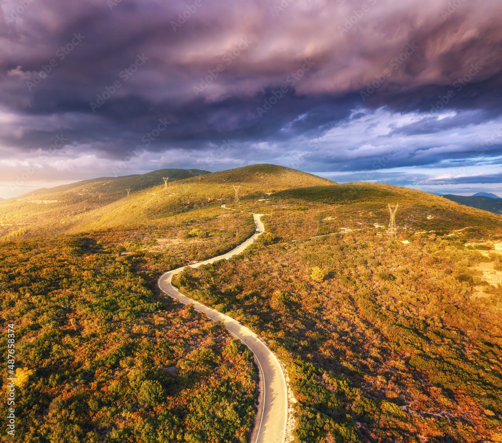 Aerial view of mountain road, green forest, dramatic overcast sky at sunset in summer in Greece. Top