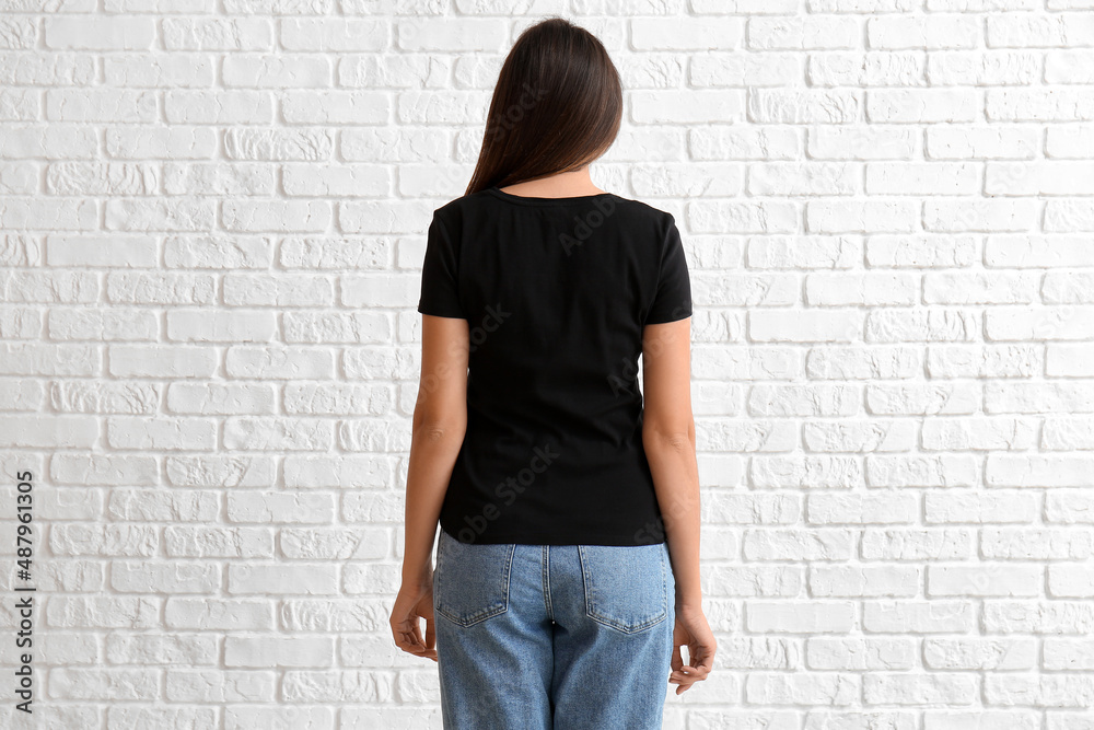 Young woman in blank t-shirt on white brick background, back view