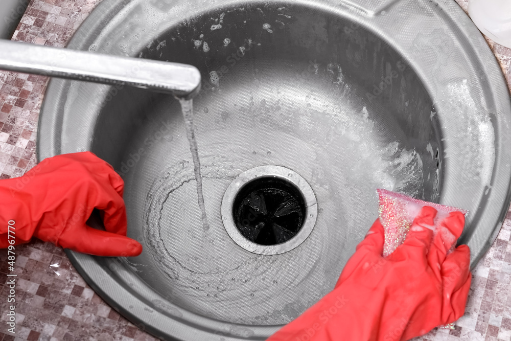 Housewife in rubber gloves cleaning silver sink with sponge, closeup