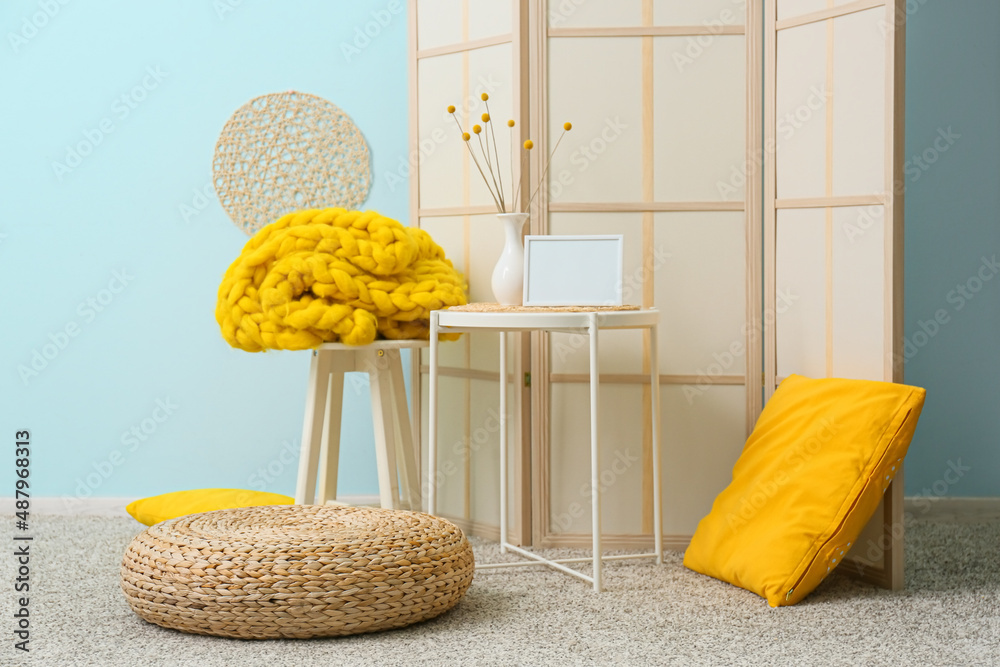 Interior of stylish room with rattan pouf, table and folding screen