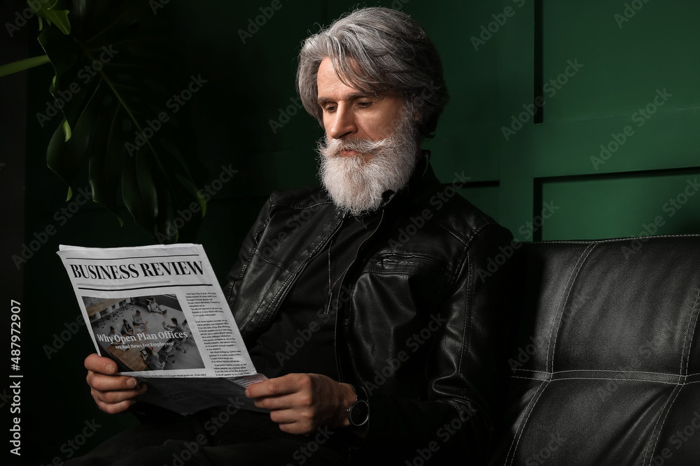 Handsome mature bearded man reading newspaper at home