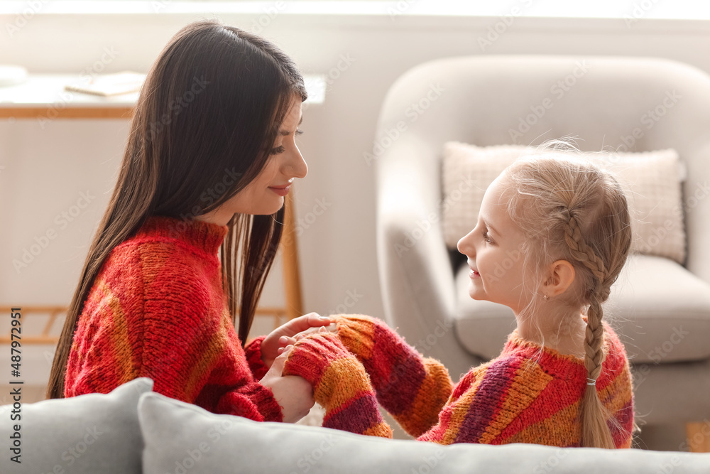 Little girl and her mother in warm sweaters holding hands at home