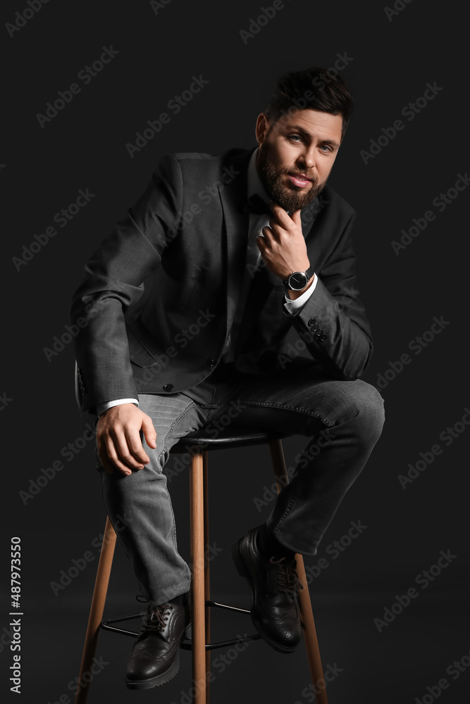 Stylish bearded man sitting on chair against dark background