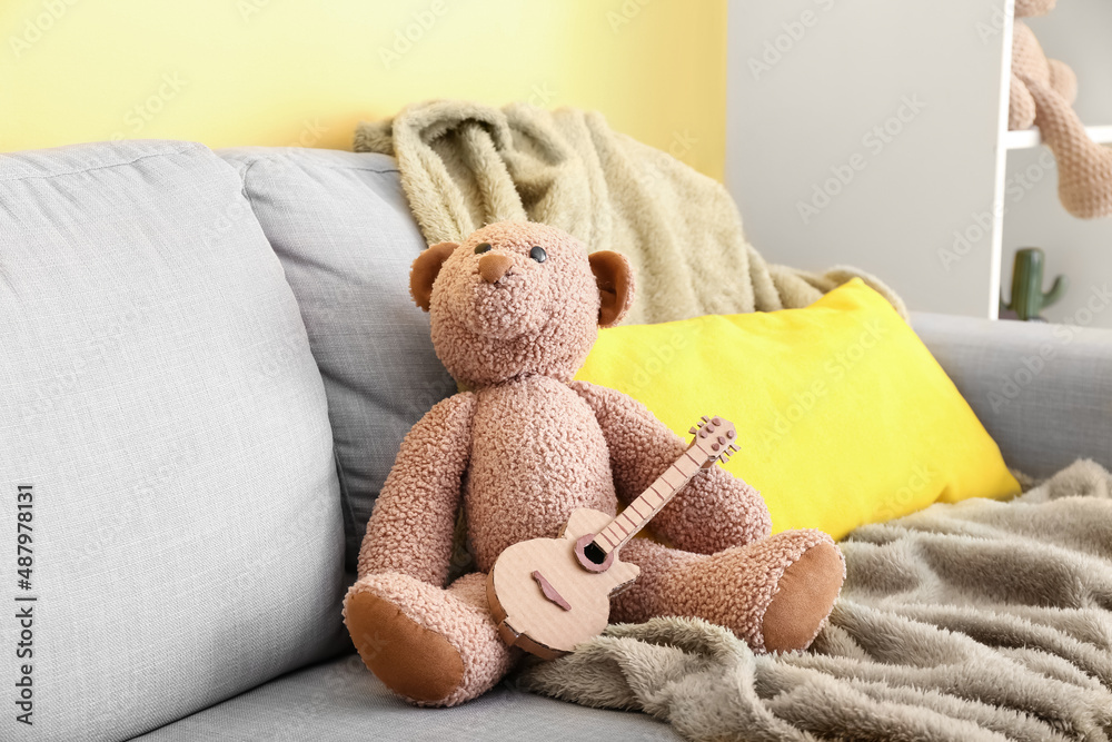 Toy bear with cardboard guitar on sofa in room