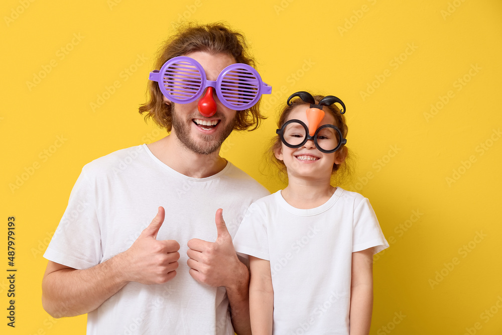 黄色背景下的滑稽男子和她的小女儿乔装打扮。愚人节庆祝活动