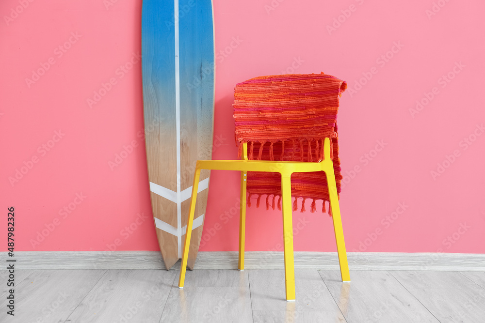 Wooden surfboard and chair with rug near pink wall