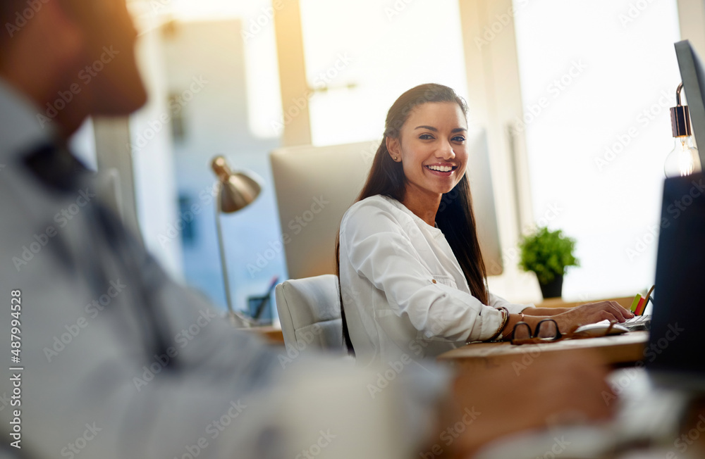 The dynamic in the office always makes her happy. Shot of a young woman working in an office.