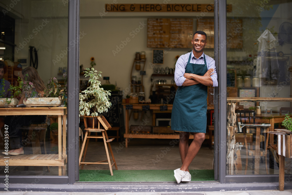 为我的店铺感到骄傲。一个英俊的年轻人站在他的店铺门口。