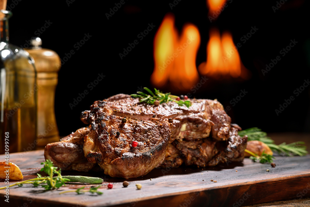 Cooked juicy steak meat beef with seasoning on wooden chopping board with flames in the background.