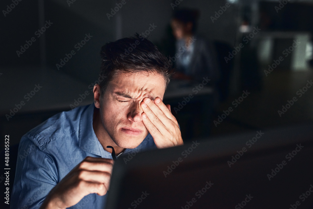 How can I be productive with this headache. Shot of a young businessman working late at night in a m