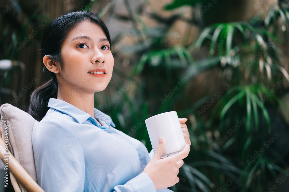 Beautiful young Asian woman relaxing in the garden and drinking tea