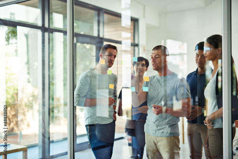 Planning is the first step. Cropped shot of a group of young designers planning on a glass board.