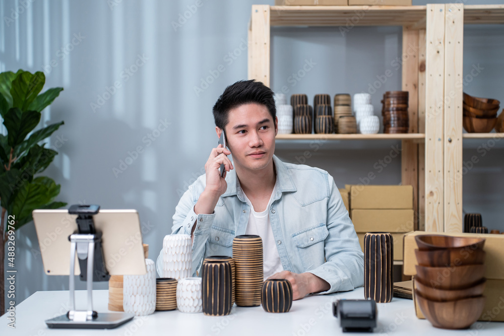 Asian young man talk with customer on phone to check vase goods order. 