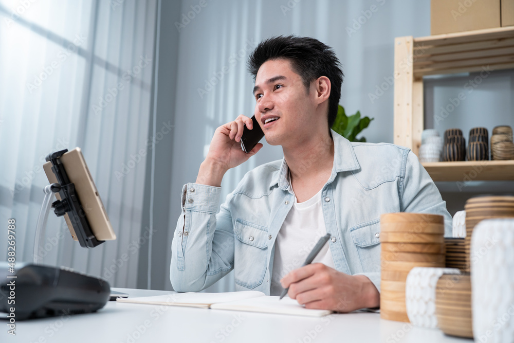 Asian young man talk with customer on phone to check vase goods order. 