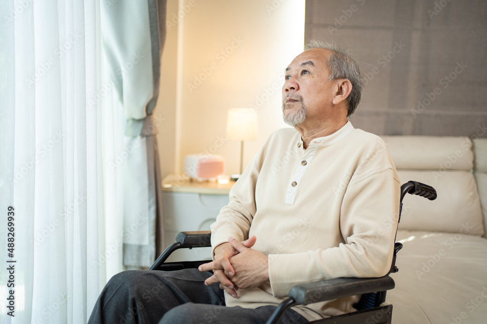 Asian senior elderly male sitting on wheelchair in living room at home. 