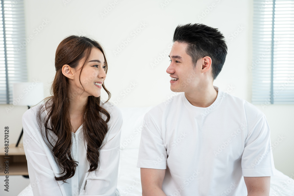 Portrait of Asian new marriage couple sit on bed and look each other. 