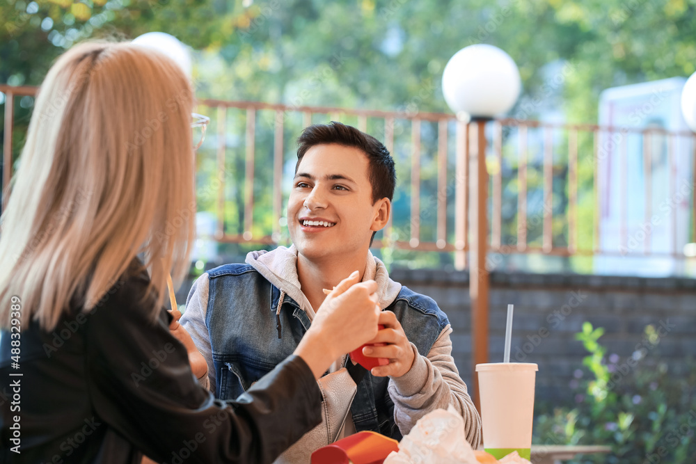 Young couple eating french fries in cafe outdoors