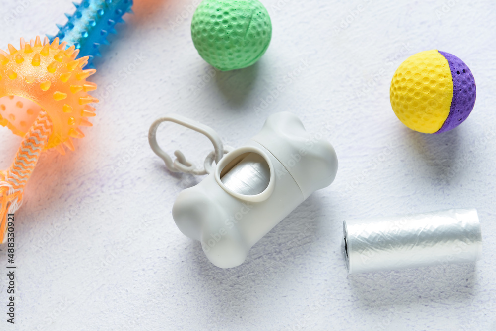 Dispenser with pet waste bags and toys on light background, closeup