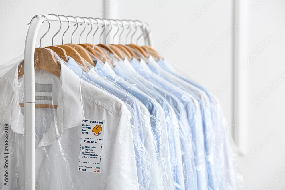 Rack with clean shirts in plastic bags near light wall