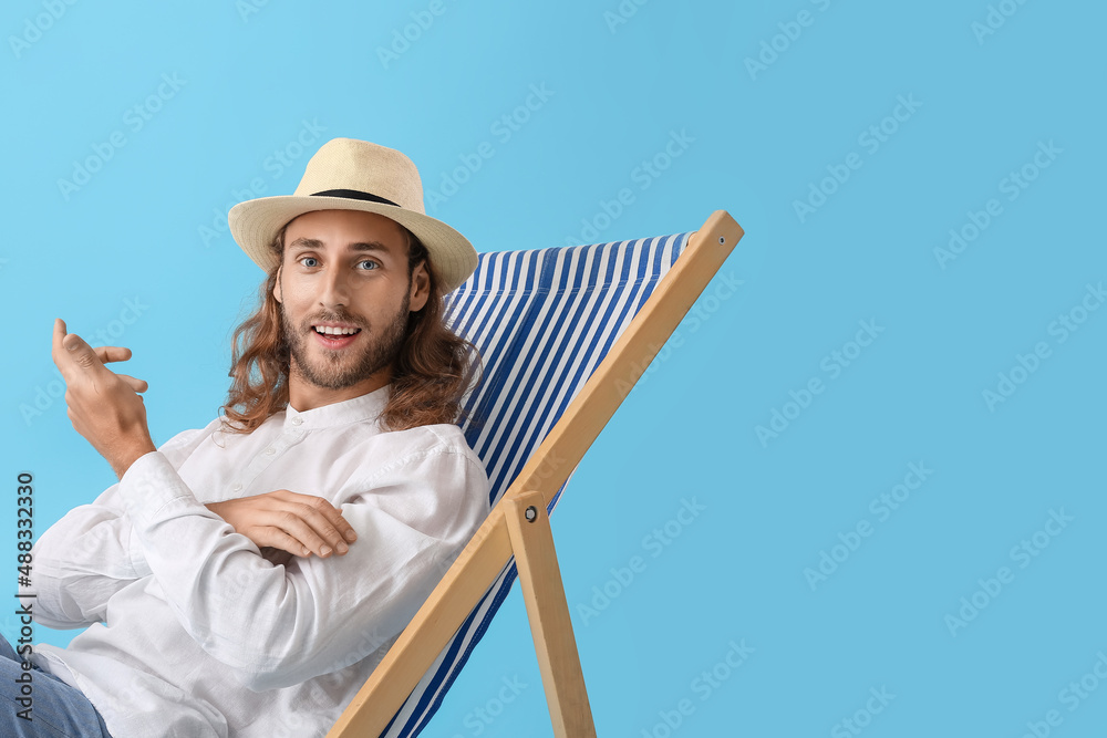 Handsome young man sitting on deck chair against color background