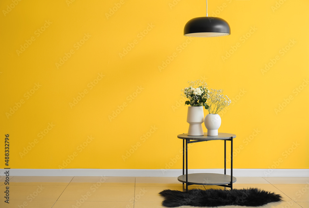 Vases with roses and gypsophila flowers on table near yellow wall