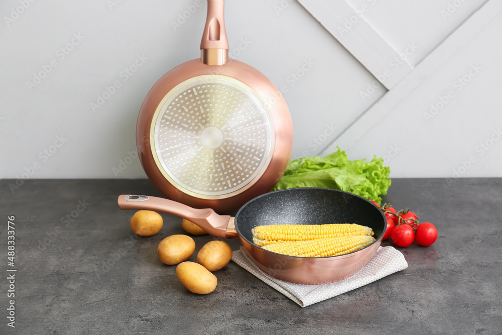 Frying pans and ingredients on table near light wall