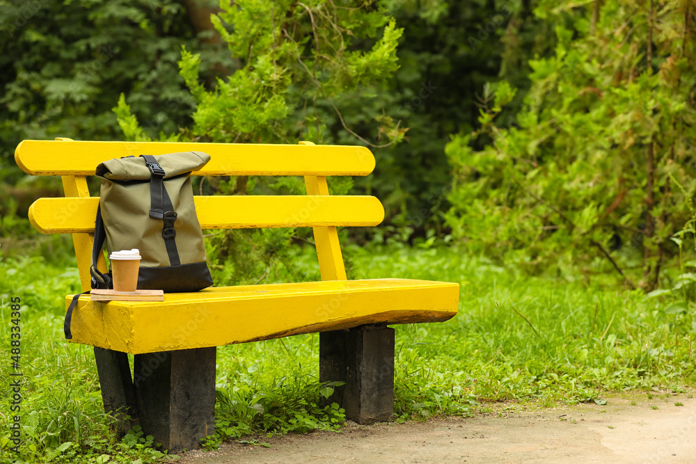 Tourists backpack, book and coffee on bench in park