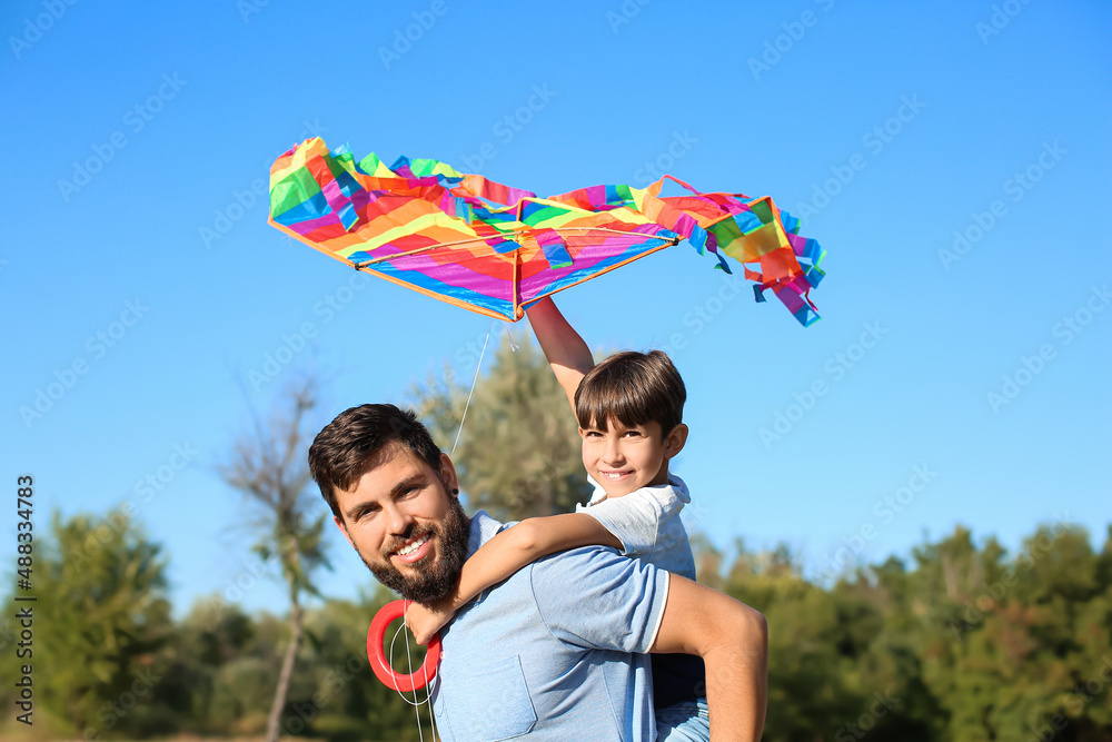 Happy father carrying pickaback his little son with kite in park