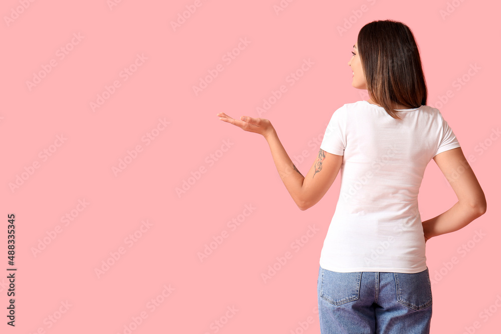 Young woman in blank t-shirt showing something on color background, back view