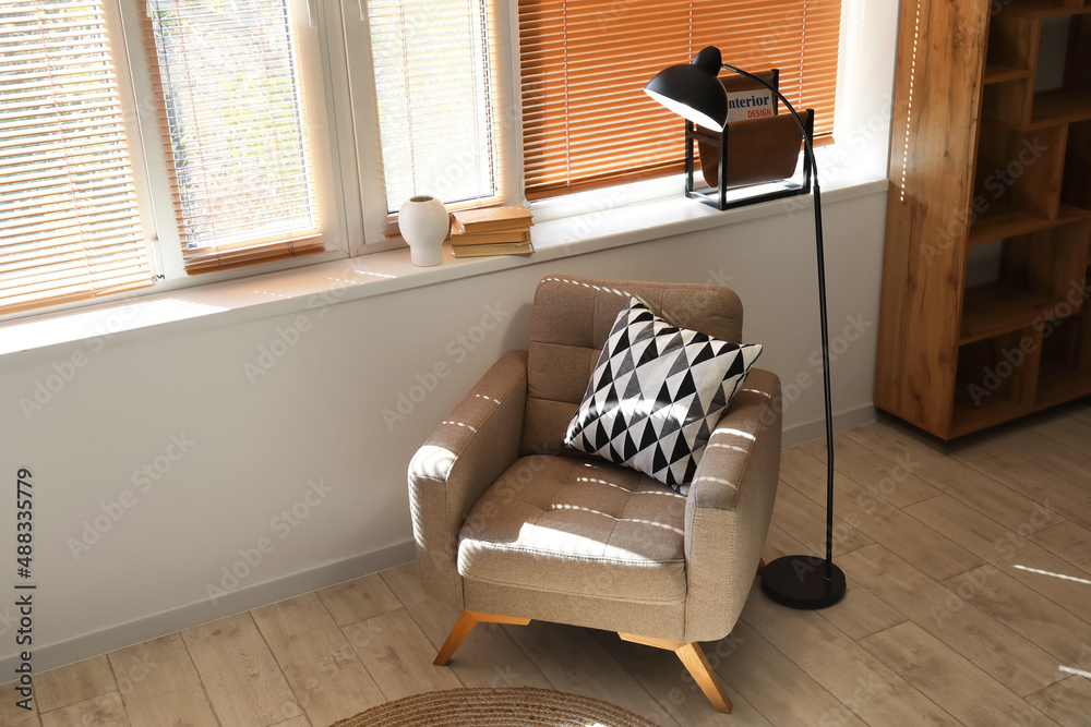 Comfortable armchair and glowing lamp near window