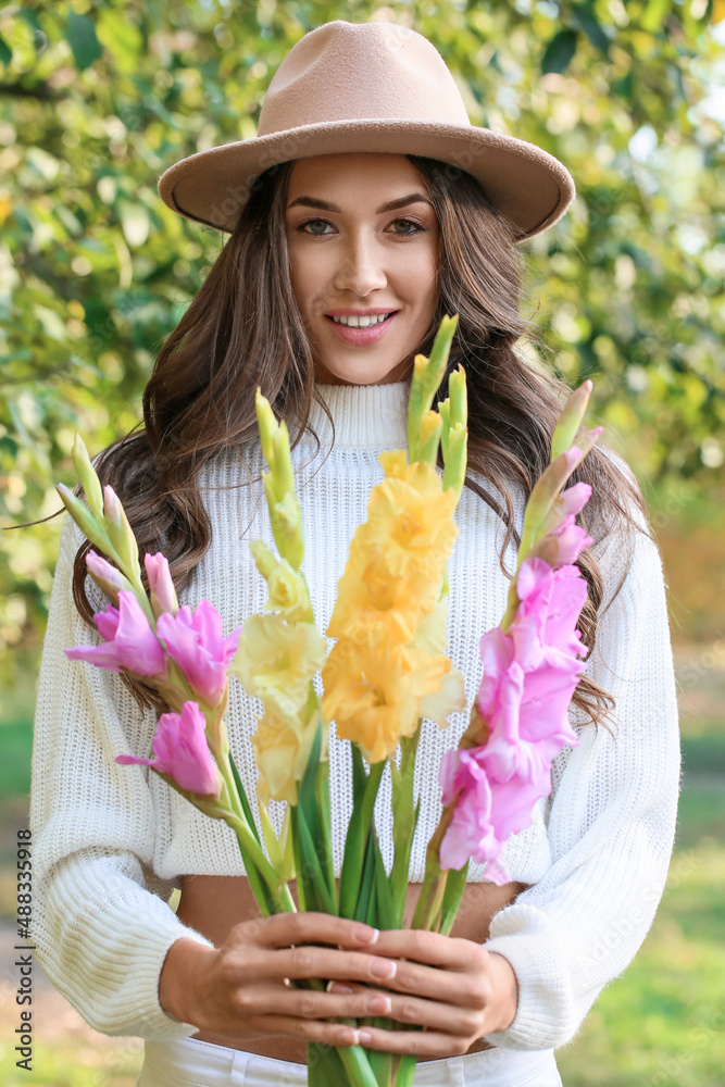 Young fashionable woman with beautiful bouquet of Gladiolus flowers in park