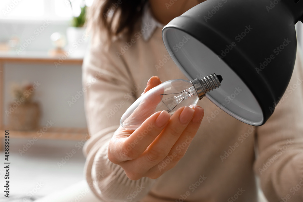 Woman changing light bulb in black lamp at home, closeup