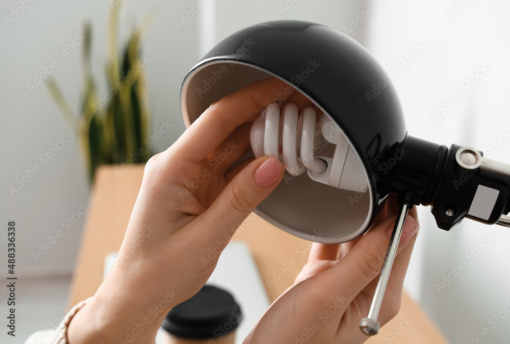 Woman changing light bulb in black lamp at workplace, closeup