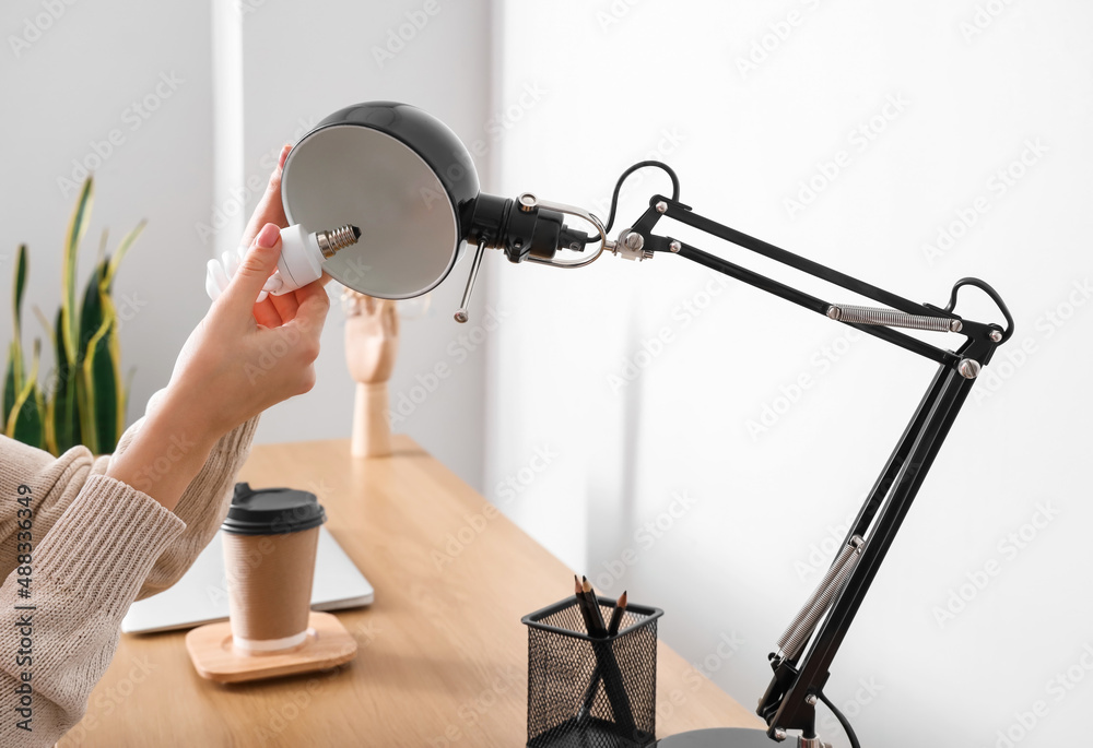 Woman changing light bulb in black lamp at workplace, closeup