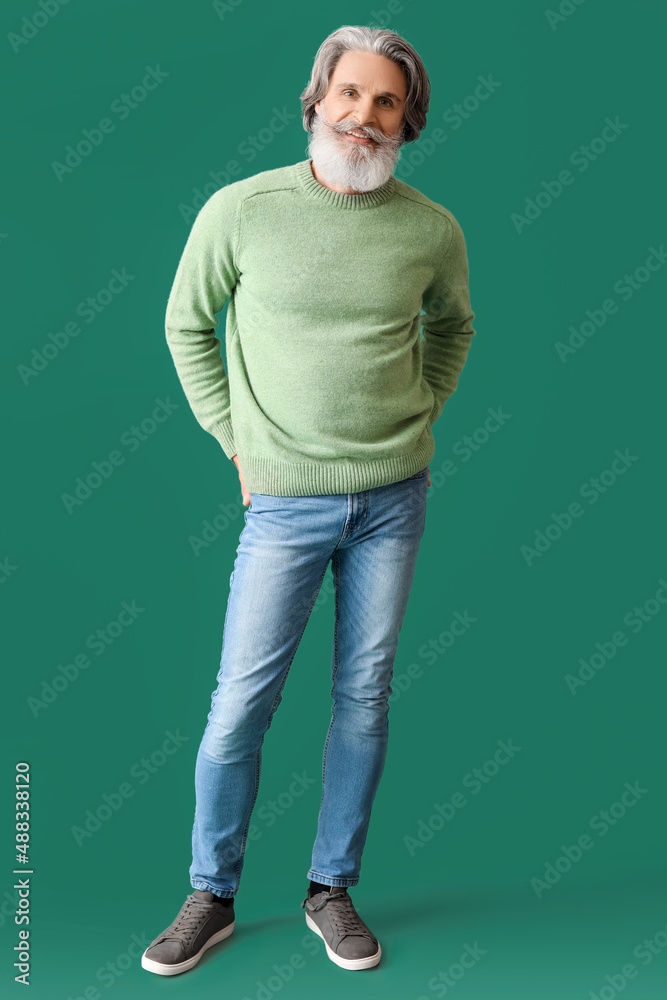 Handsome senior man in knitted sweater on green background