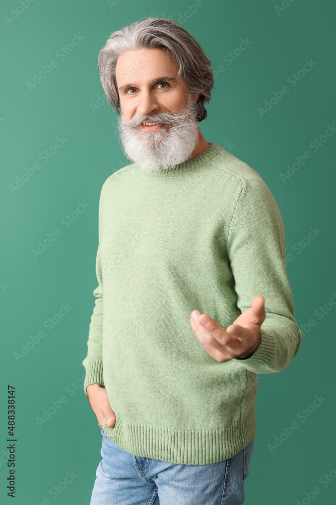 Handsome senior man in knitted sweater on green background