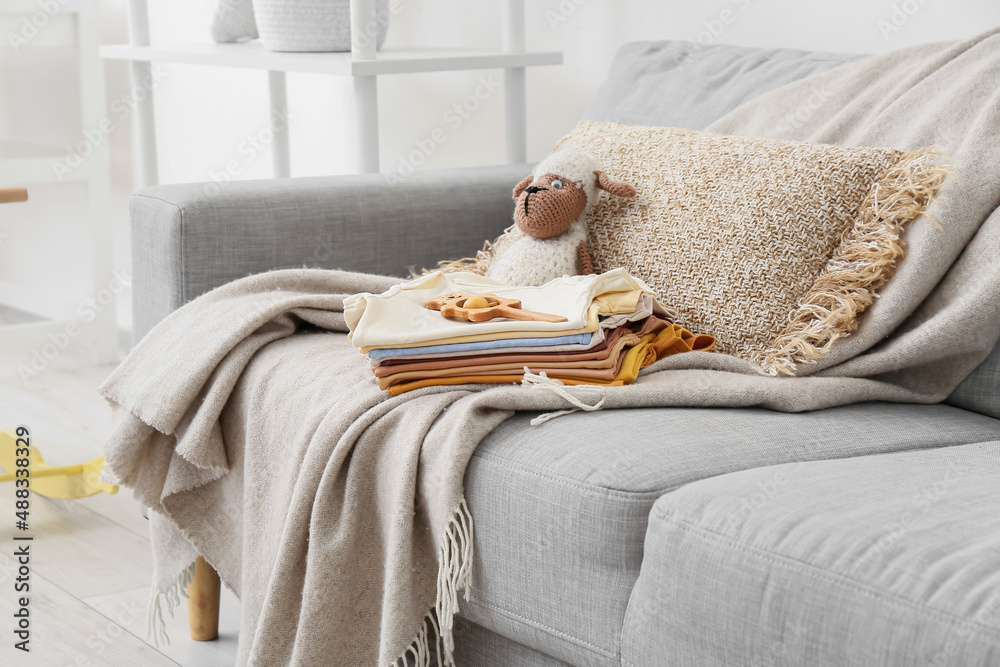 Stack of baby clothes and toys on comfortable sofa in living room