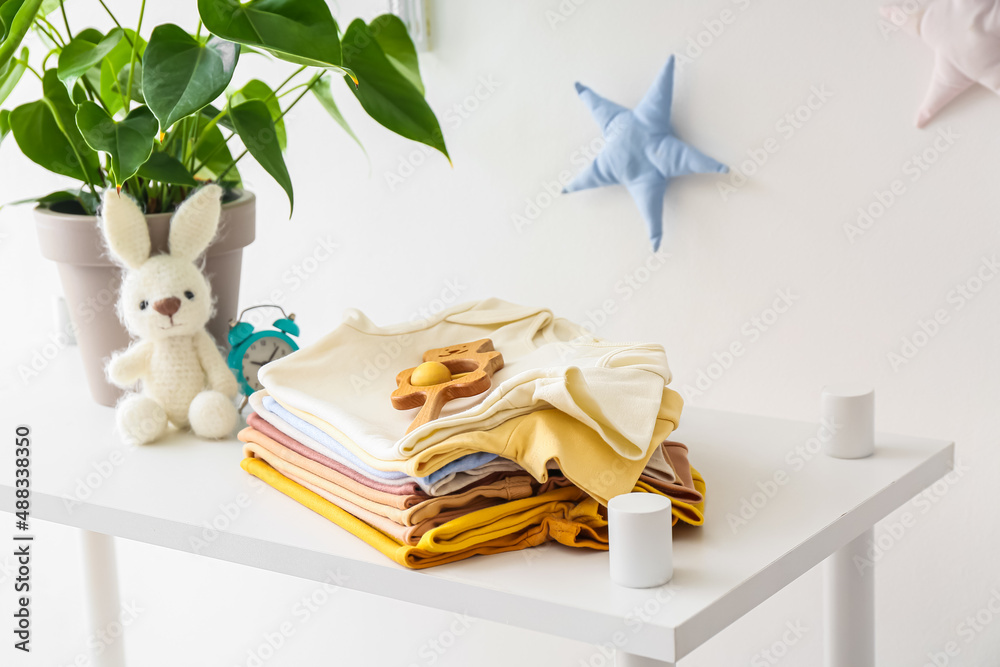 Stack of baby clothes, toys and houseplant on self unit near light wall