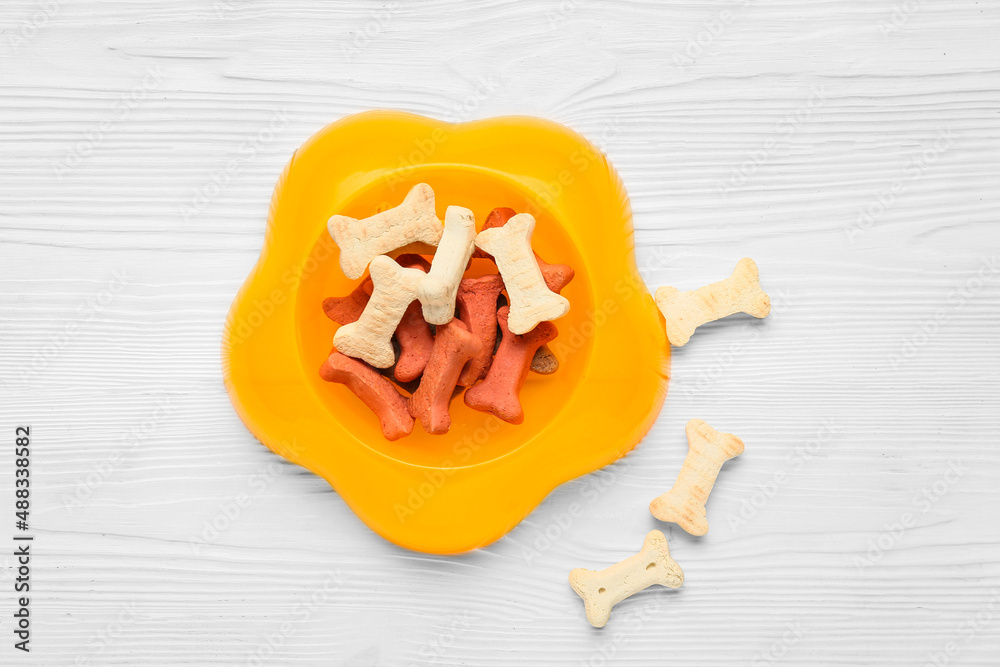 Bowl of tasty snacks for pet on white wooden background