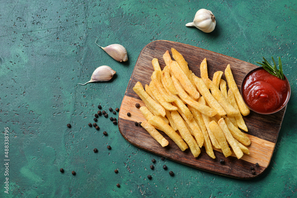 Wooden board with tasty french fries and ketchup on green background